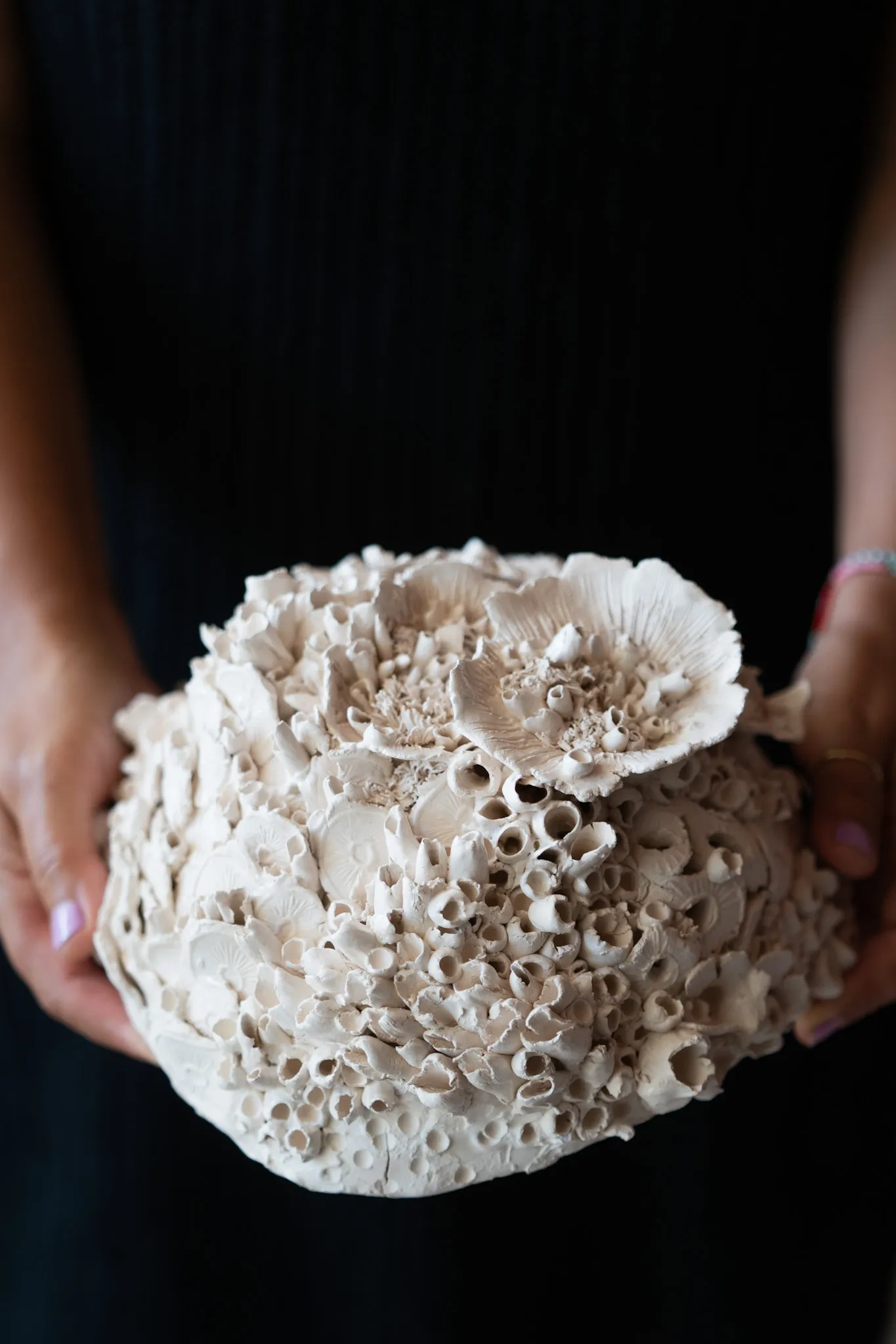 Domed ceramic reef form held in two hands against a black top. Tightly packed tubes rise to a large ruffled disc at the crown.